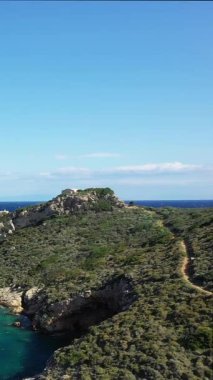 Yunanistan 'ın Porto Kagio kentindeki berrak gökyüzünün altında yemyeşil bitki örtüsü ve derin mavi denize sahip engebeli bir sahil manzarası.