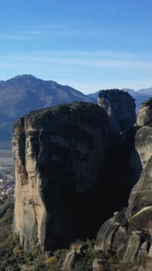 Yunanistan 'ın Meteora kentindeki manzara üzerinde yükselen etkileyici dikey kaya kayalıkları, açık mavi gökyüzünün altındaki uzak dağlarla birlikte. Eşsiz bir jeolojik mucize ve doğal bir dönüm noktası..