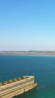 Sakin denizin üzerindeki açık mavi gökyüzü Gold Beach, Asnelles, Normandiya, Fransa 'da tarihi yapay liman yapısı. Uzak kıyı şeridi ve canlı su ile sakin kıyı manzarası.