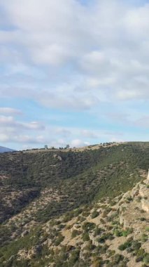 Yunanistan 'ın Hermione kentinin kırsal kesiminde, parçalı bulutlu bir gökyüzü altında çalılarla ve kayalık çıkıntılarla kaplı yuvarlanan tepelerin geniş bir manzarası.