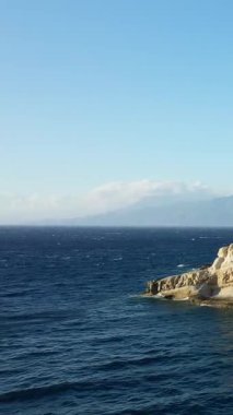 Girit Matala, Girit 'te derin mavi Akdeniz' le buluşan engebeli kireçtaşı kayalıkların manzarası, berrak bir gökyüzü altında uzak dağlar..