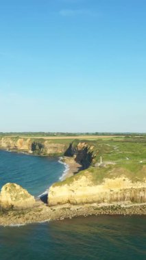Fransa 'nın Normandiya bölgesindeki Pointe du Hoc kentindeki engebeli kıyı şeridi ve dramatik uçurumların havadan görünüşü. Sahnede kayalık kıyılar, yeşil alanlar ve geniş deniz yer alıyor..