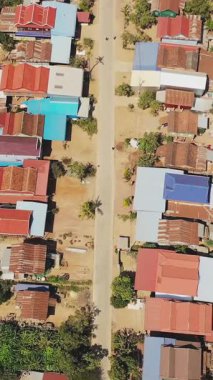 Renkli çatılar ve Kamboçya 'nın Phnom Penh yakınlarındaki küçük evlerle çevrili düz bir yolun insansız hava aracı görüntüsü. Sahne, kırsal yerleşim yerlerinin ve doğal elementlerin açık bir planını içeriyor..
