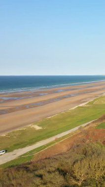 Fransa 'nın Normandiya şehrinde kumlu kıyı şeridi, yeşil tarlalar ve açık mavi gökyüzünün altındaki uzak uçurumlar geniş bir görüş alanına sahip..