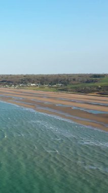 Açık mavi gökyüzü altında gelgit havuzları, kumlu kıyılar ve yeşil kırsal manzaralı Omaha Sahili. Sakin deniz manzarası, Normandiya kıyılarının doğal güzelliğini vurgular..
