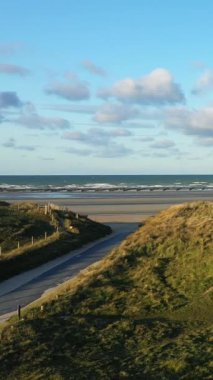 Çimenli kum tepelerinin manzarası ve denize giden dolambaçlı bir yol Utah Beach, Normandiya, Fransa 'da mavi bir gökyüzünün altında..