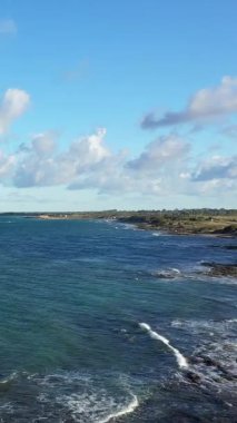 İtalya 'nın Brindisi kenti yakınlarında engebeli bir kıyı şeridi, mavi deniz ve dağınık bulutlar görülüyor. Açık gökyüzü ve yumuşak dalgalarla doğal deniz manzarası.