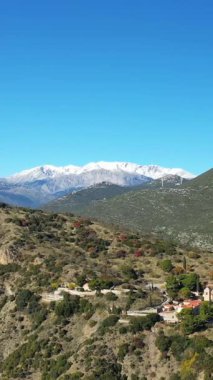 Yunanistan 'da açık mavi bir gökyüzünün altında, arka planda karla kaplı dağlarla dolu yemyeşil bir vadide yuva yapmış tarihi Osios Loukas Manastırı' nın havadan görünüşü.