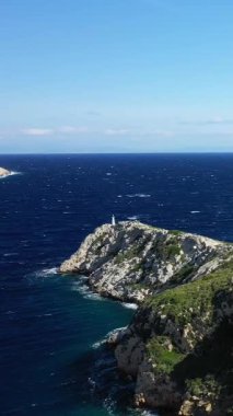 Yunanistan 'ın Porto Kagio kentinde açık bir gökyüzü altında, yemyeşil tepelerin derin mavi denizle buluştuğu dramatik kayalık kıyı şeridi.