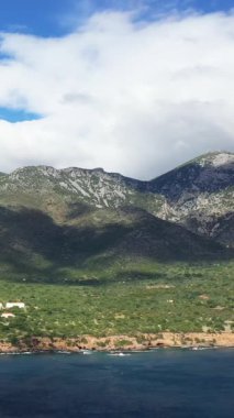 Yunanistan 'ın Monemvasia kenti yakınlarındaki kıyı şeridi boyunca uzanan engebeli dağların manzarası, parçalı bulutlu bir gökyüzü altında.