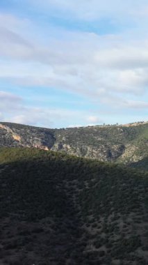 Hermione yakınlarında, parçalı bulutlu bir gökyüzü altında yeşil yuvarlanan tepelerin ve engebeli arazinin manzarası. Doğal, el değmemiş manzara doğa ve seyahat temaları için ideal..