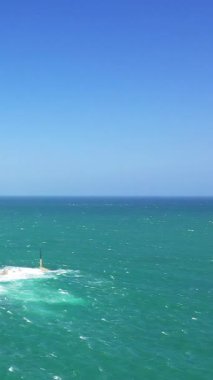 Açık mavi gökyüzünün altında canlı turkuaz okyanus dalgaları, Fransa 'nın Normandiya, Cap de la Hague yakınlarında uzak bir yön bulucu ile.