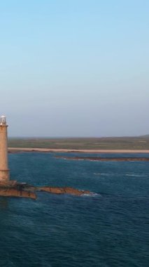 Fransa 'nın Normandiya eyaletinde, Cap de la Hague' deki kayalık bir çıkıntıda duran deniz fenerinin sakin mavi suları ve berrak bir gökyüzünün altındaki uzak kıyı şeridi manzarası.