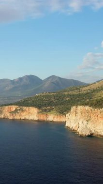 Scenic view of rugged cliffs and clear blue sea with mountains in the background near Diros Beach, Mani Peninsula, Greece. Bright daylight and natural landscape.