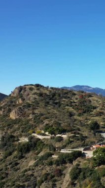 Yunanistan 'daki tarihi Osios Loukas Manastırı yakınlarında, açık mavi bir gökyüzünün altında, dağılmış ağaçlarla ve binalarla güneşli bir tepenin manzarası.