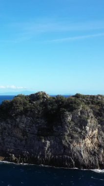 İtalya, Capo di Conca 'da açık bir gökyüzünün altında, derin mavi denizin üzerinde yeşilliklerle kaplı engebeli kayalık bir uçurum yükselir. Sakin kıyı manzarası doğal güzelliği ve Akdeniz manzarasını ön plana çıkarıyor..