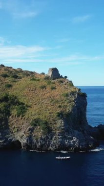 İtalya 'nın Capo Palinuro kentindeki mavi denize bakan antik taş kulesiyle sahili uçurum. Küçük bir tekne engebeli arazinin altında sakin sularda yüzer..