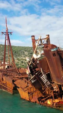 Yunanistan 'ın Gythio kenti yakınlarındaki turkuaz sularda paslanmış Dimitrios' un enkazının yakın plan görüntüsü. Arka planda parçalı bulutlu bir gökyüzünün altında yeşil tepeler var..