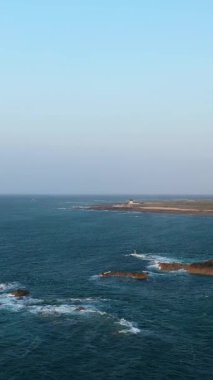 Cap de la Hague, Normandiya, Fransa 'daki engebeli kıyı şeridi ve mavi denizin geniş görüşü, açık bir gökyüzü altında kayaların üzerinde dalgaların kırılışıyla.