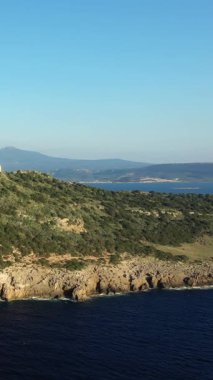 Yunanistan 'ın Navarino kenti yakınlarında berrak bir gökyüzü altında kayalık uçurumlar, yemyeşil yemyeşil ve derin mavi deniz manzarası.