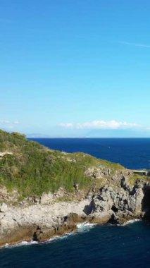 Kayalık kıyı şeridinin manzarası ve açık mavi deniz Capo di Conca, İtalya 'da, parlak bir gökyüzünün altında. Yeşillik sudaki kayalıkları kaplıyor..