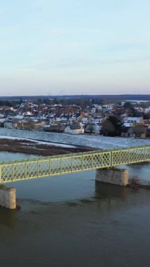 Arka planda Sully sur Loire kasabası olan bir nehri geçen sarı bir köprünün manzarası. Bir kış günü çatılar karla kaplanmış..