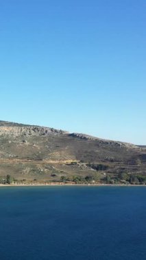 Paralia Karathona, Nauplie, Yunanistan 'da parlak bir gökyüzü altında berrak mavi sular ve engebeli tepelerle dolu sakin bir kıyı şeridi..