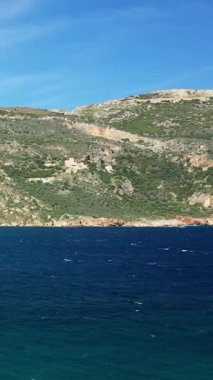 Yunanistan 'da Porto Kagio kıyı şeridi boyunca uzanan engebeli tepeleri ve dağınık evleri olan berrak mavi deniz parlak bir gökyüzü altında.