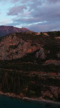 Yunanistan 'ın Kardamyli kentinde gün batımında engebeli kıyı şeridi ve dağ yamaçlarının manzarası, dramatik bulutlar ve sakin deniz seviyesiyle.