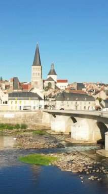 La Charite-sur-Loire 'ın ikonik kilise kulesi, geleneksel binaları ve Loire Nehri üzerindeki açık mavi gökyüzünün altındaki taş köprüsü manzarası..