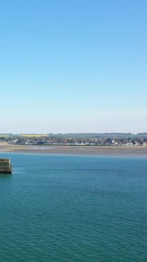 Asnelles, Normandiya, Fransa 'nın kumlu kıyı şeridi yakınlarındaki durgun mavi sudaki yapay liman yapısını parlak mavi bir gökyüzünün altında net bir şekilde görebiliriz..