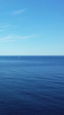 İtalya 'nın Capo Palinuro kenti yakınlarındaki berrak bir gökyüzünün altındaki sakin mavi denizde tek başına yelkenli görüntüsü. Açık deniz ve uzak ufukta sakin bir deniz manzarası.