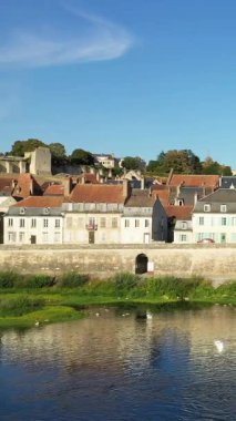 Fransa 'nın La Charite-sur-Loire kentindeki nehir kıyısında, açık mavi gökyüzünün altında kırmızı kiremitli çatıları olan büyüleyici eski evler. Huzurlu manzara, kasabaların geleneksel mimarisini ve sakin sahil manzarasını yakalıyor..