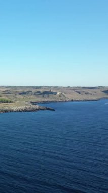 İtalya 'nın Porto Badisco şehrinde kayalık kıyı şeridi ve açık bir gökyüzünün altında derin mavi deniz manzarası. Sakin suyu ve engebeli arazisi olan doğal kıyı manzarası.