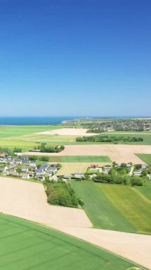 Normandiya kıyı şeridinin dramatik uçurumları, yamalı arazileri ve açık mavi gökyüzünün altındaki küçük bir köy manzarası. Canlı manzara, Kuzey Fransa 'nın doğal güzelliklerini yansıtıyor..