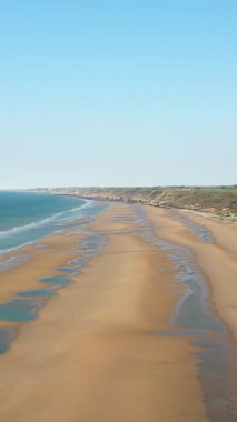Omaha Sahili 'nin geniş manzarası. Altın kum, yumuşak dalgalar ve Fransa' nın Normandiya şehrinde açık mavi bir gökyüzü. Sahil şeridi yeşil kayalıklarla çevrili kıyı boyunca uzanır..