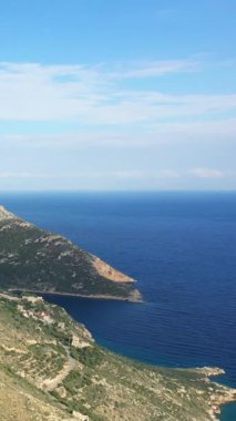 Yunanistan 'da parlak bir gökyüzü altında berrak mavi deniz ve geleneksel taş evlerle engebeli Mani Yarımadası kıyı şeridinin manzarası.