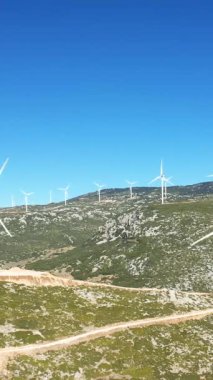 Yunanistan 'ın Thisbe kenti yakınlarındaki açık mavi gökyüzünün altındaki kayalık, yeşil tepelerde çok sayıda rüzgar türbini duruyor. Akdeniz 'de yenilenebilir enerji manzarası.