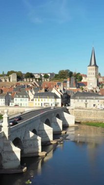 Loire Nehri 'nden geçen tarihi bir taş köprünün manzarası. Geleneksel binalar ve Fransa' nın La Charite-sur-Loire şehrinde açık mavi gökyüzünün altında bir kilise kulesi..