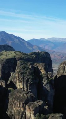 Meteora 'nın görkemli kayalık kayalıkları, Yunanistan' da açık mavi bir gökyüzünün altındaki uzak dağ zeminine doğru yükseliyor. Çarpıcı jeolojik oluşumları ve verimli yeşilliği olan doğal manzara..
