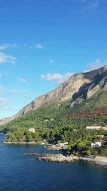 Bereketli yeşillik, kayalık uçurumlar ve parlak bir gökyüzünün altındaki açık mavi deniz manzaralı Maratea sahili. Resimli manzara İtalyan sahilinin doğal güzelliğini vurguluyor..