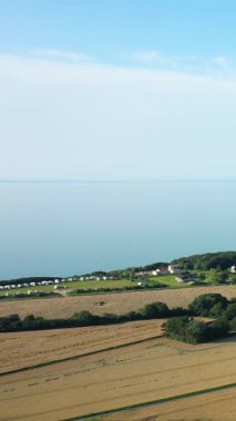 Fransa 'nın Veules les Roses yakınlarındaki sahil şeridi boyunca açık mavi bir gökyüzünün altında, tarlaların, yeşilliklerin ve bir kamp alanının havadan görünüşü..