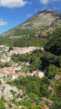 Lauria 'nın manzarası, yemyeşil tepeler ve parlak mavi gökyüzünün altındaki dağların arasına kurulmuş büyüleyici bir İtalyan köyü. Doğal güzelliklerle çevrili terasotta çatıları olan resimli evler..