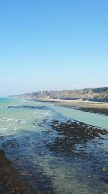 Normandiya 'nın Port en Bessin kıyısındaki kayalık kıyı şeridi ve turkuaz sularının berrak mavi gökyüzünün altında manzarası..