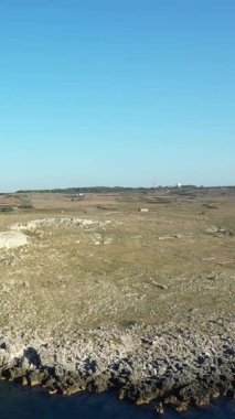İtalya 'nın Porto Badisco kentindeki açık mavi gökyüzünün altında kayalık bir kıyı şeridi ve kurak bir arazi manzarası. Engebeli kıyı manzarası doğal dokular ve açık alanla vurgulanır..