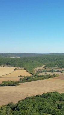 Fransa 'nın Varzy şehrinde, Cuncy les Varzy yakınlarında açık mavi bir gökyüzü altında, yamalı tarım arazisi ve sık bir ormanın havadan görünüşü. Huzurlu kırsal alan dağınık evler ve canlı yeşillikler..