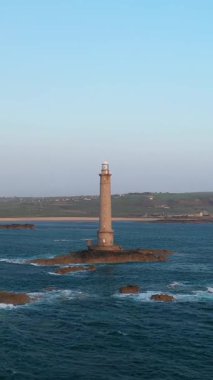 Uzun taş deniz feneri, Fransa 'nın başkenti Cap de la Hague' de uzak kıyı şeridi ve açık gökyüzü ile çevrili mavi okyanus sularıyla çevrili kayalık bir adada duruyor..