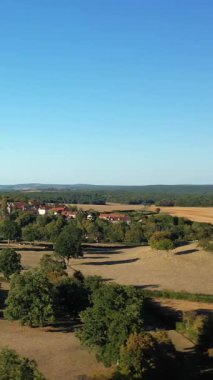 Altın tarlalar, dağınık ağaçlar ve Fransa 'nın Cuncy les Varzy yakınlarında açık mavi bir gökyüzünün altında küçük bir köy. Uzak ormanlar ve yuvarlanan tarım arazileriyle sakin bir kırsal alan..