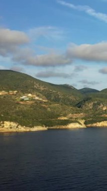 Yunanistan 'ın Syvota kentinde bulutlu bir gökyüzünün altında yemyeşil bir tepenin sakin mavi denizle buluşmasının manzarası. Dramatik uçurumları ve dingin suları olan doğal kıyı şeridi.