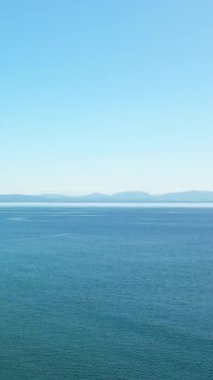 Yunanistan 'ın Gythio kenti yakınlarında berrak bir gökyüzünün altında yumuşak dalgalar ve uzak sıradağlar bulunan sakin mavi deniz. Huzurlu doğal manzara seyahat ve rahatlama temaları için ideal.